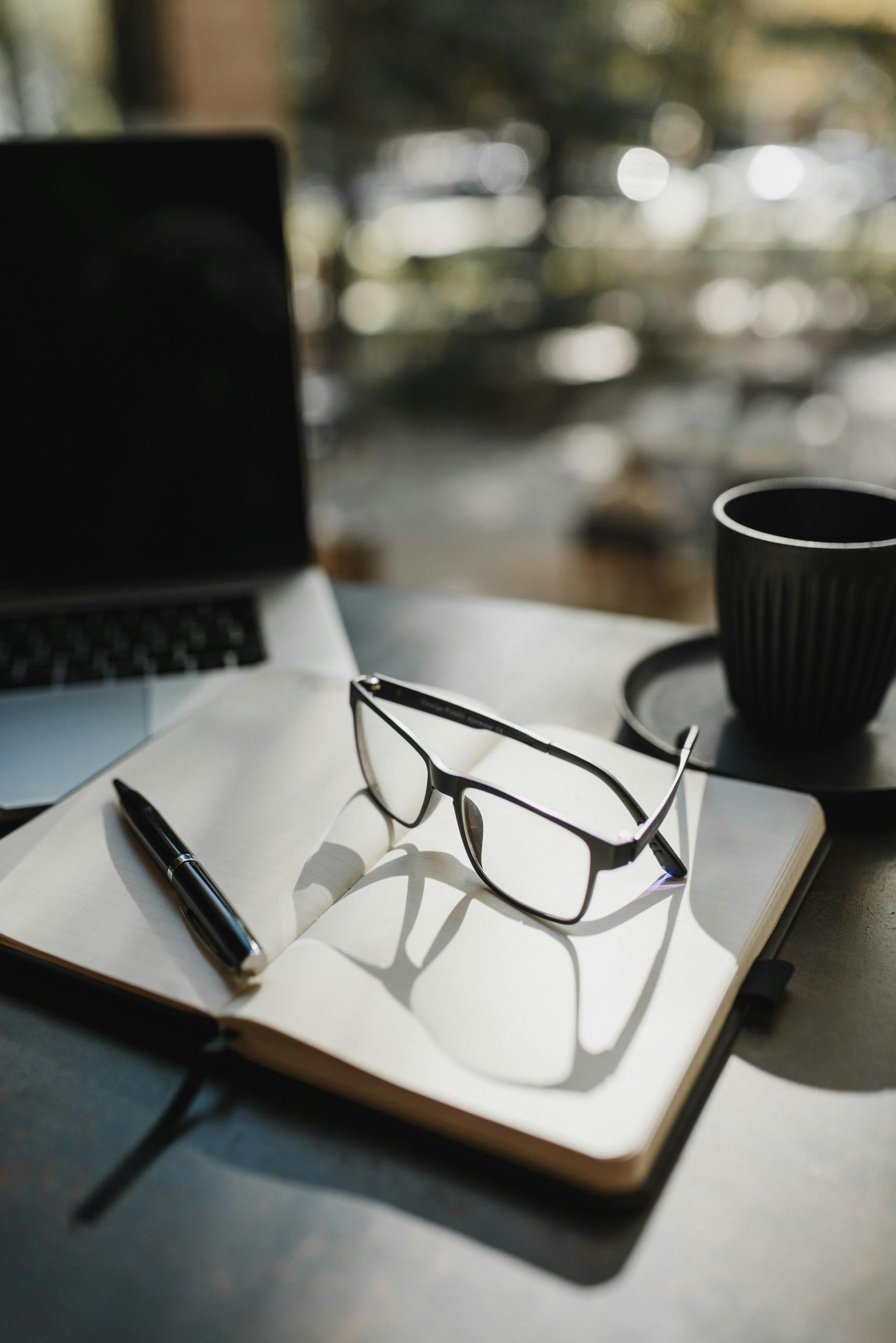 Stylish eyeglasses on an open notebook with a coffee cup, perfect for productivity and study themes.